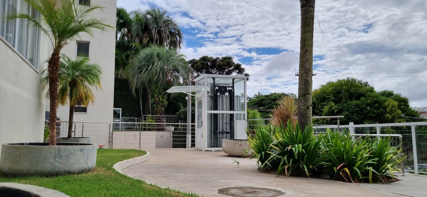 Área externa do Flat Care com paisagismo, jardins e elevador acessível